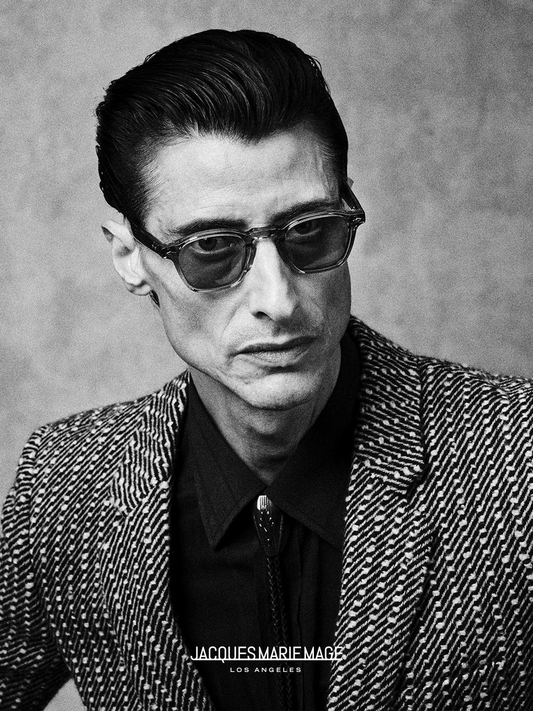 Man in sunglasses wearing a patterned blazer, against a textured background.