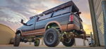 Rear three-quarter view of lifted black and copper Ram with bronze train horns mounted underneath at sunset