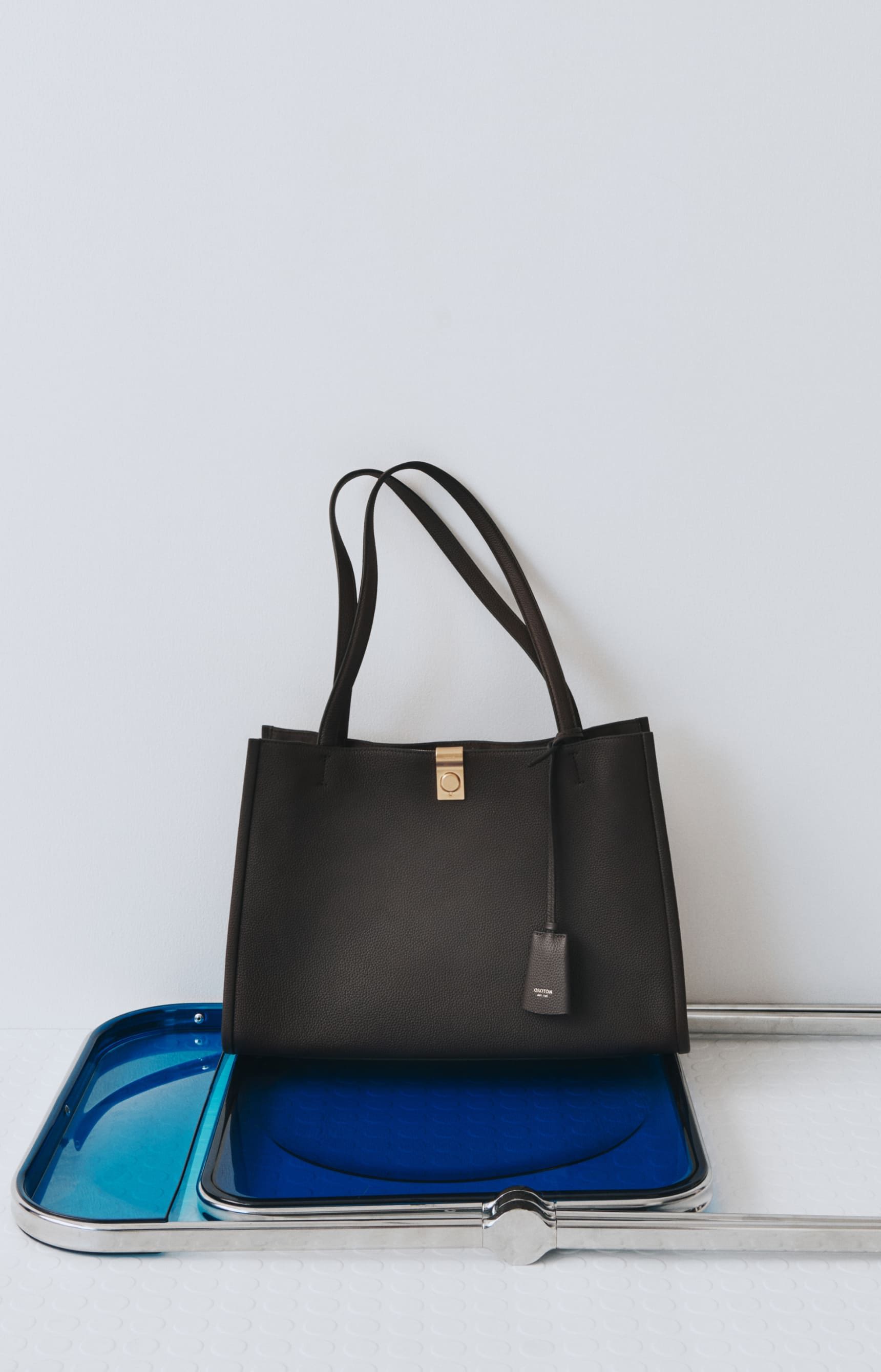 A black handbag on a blue tray against a white background.