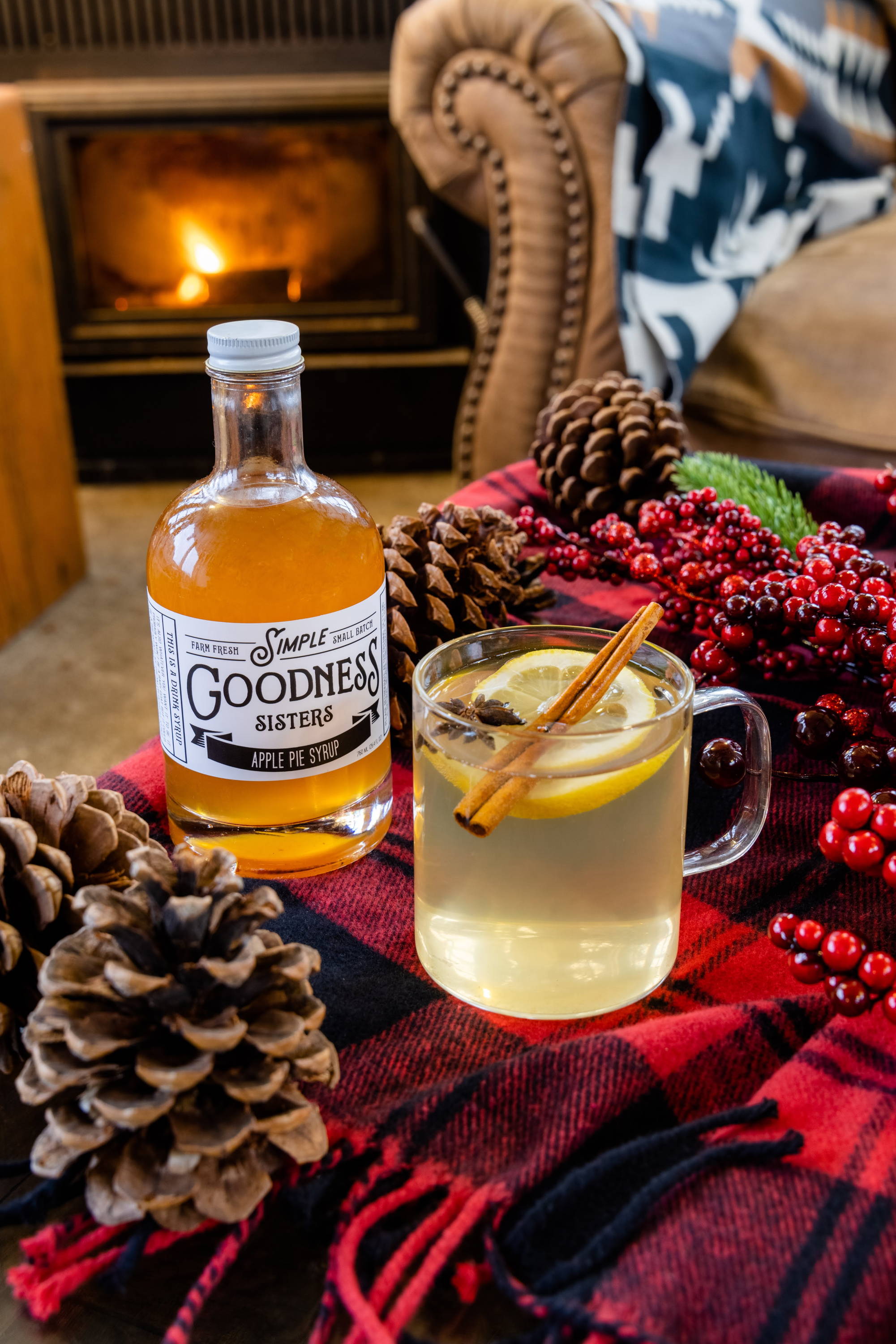 a hot toddy cocktail on a red plaid blanket in front of a fire