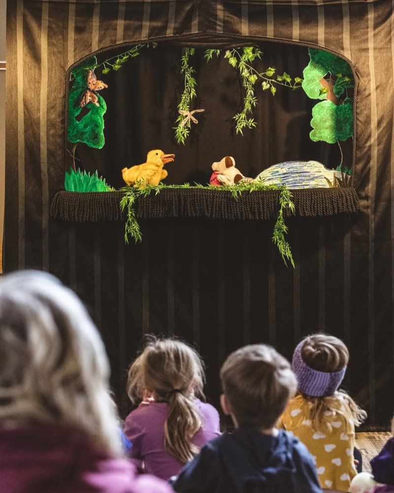 Children watching a puppet show with animal characters on stage.