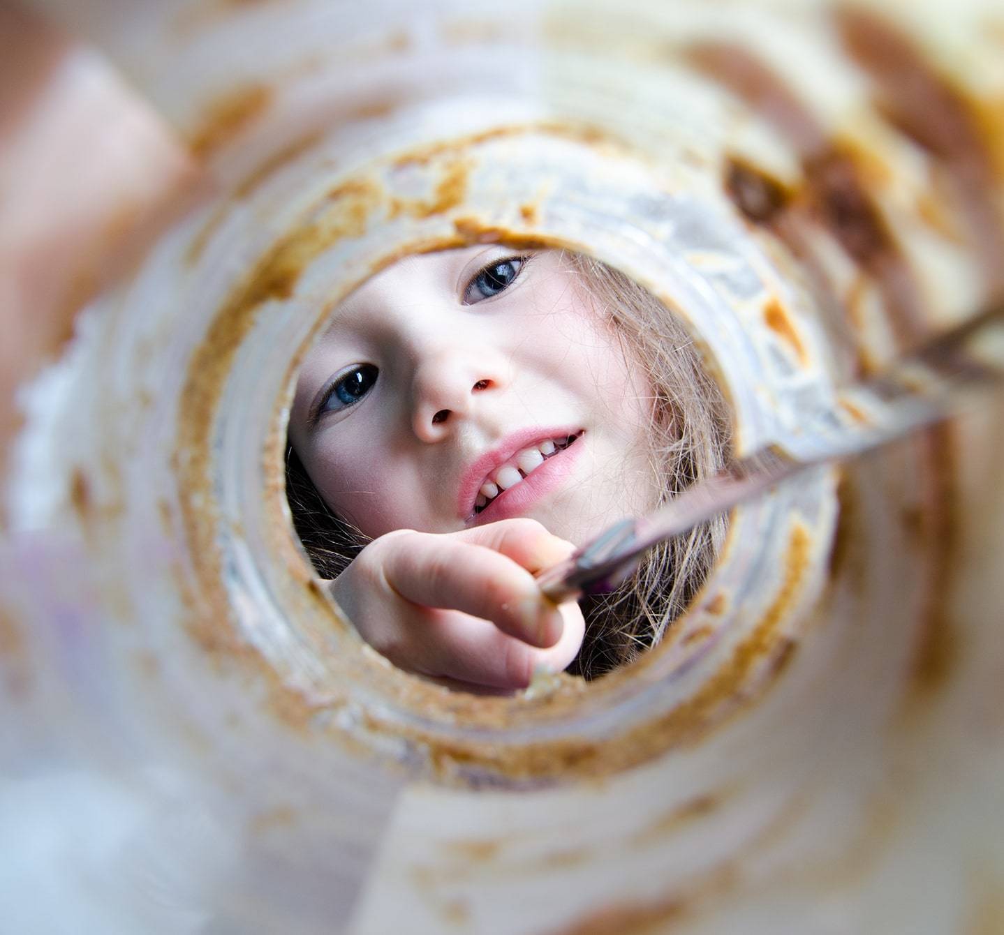 Kind, das mit einem Messer ein Erdnussbutterglas auskratzt – eine verbotene Leckerei, wenn es allergisch gegen Erdnüsse ist.