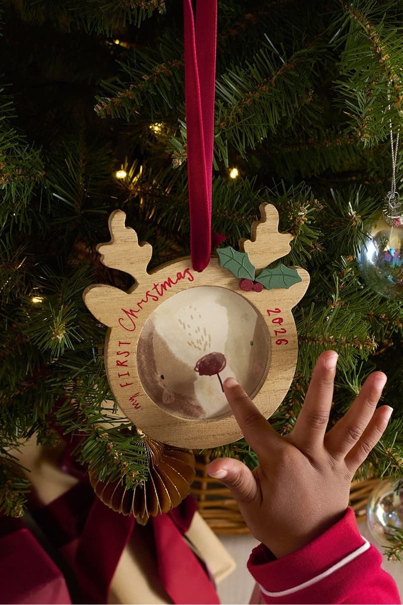 Child's hand reaching for a reindeer ornament on a Christmas tree.