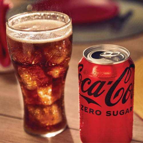 A glass of coke zero with a can beside it 