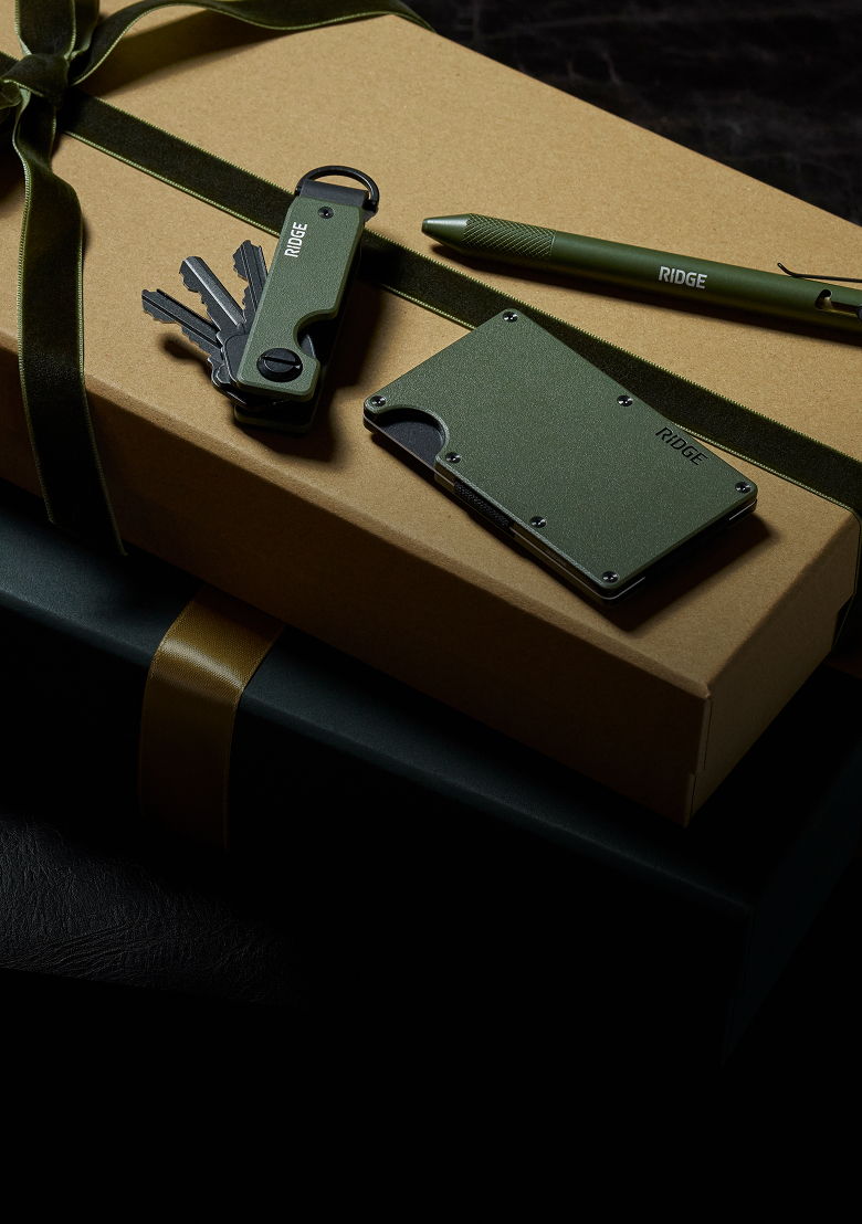 A gift box with green accessories: a wallet, multi-tool, and pen.