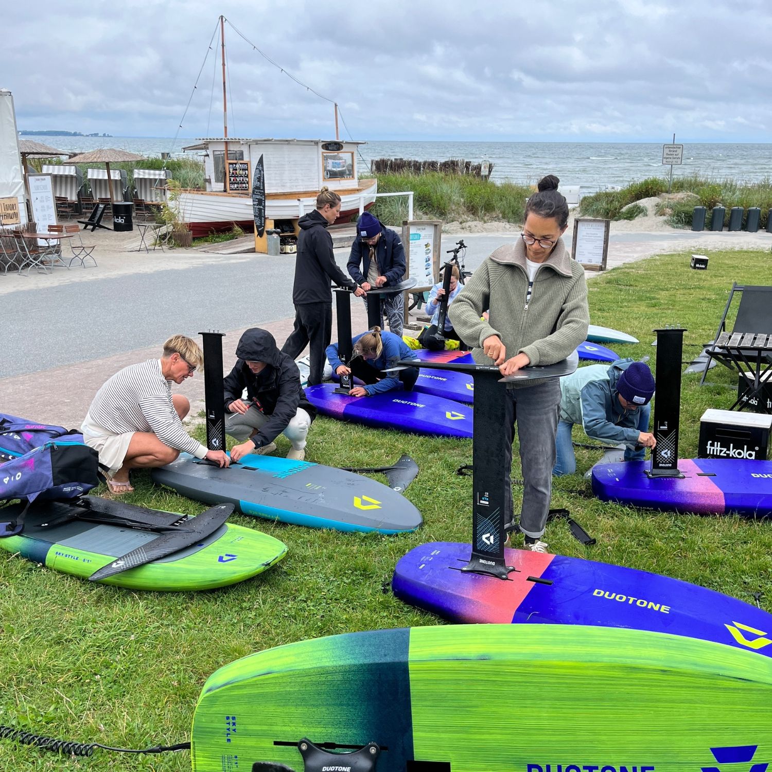 People preparing wingboards on grass near the beach.