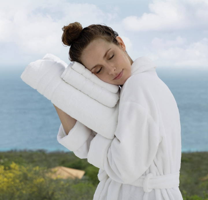 A woman holding a stack of Cariloha Bath Towels