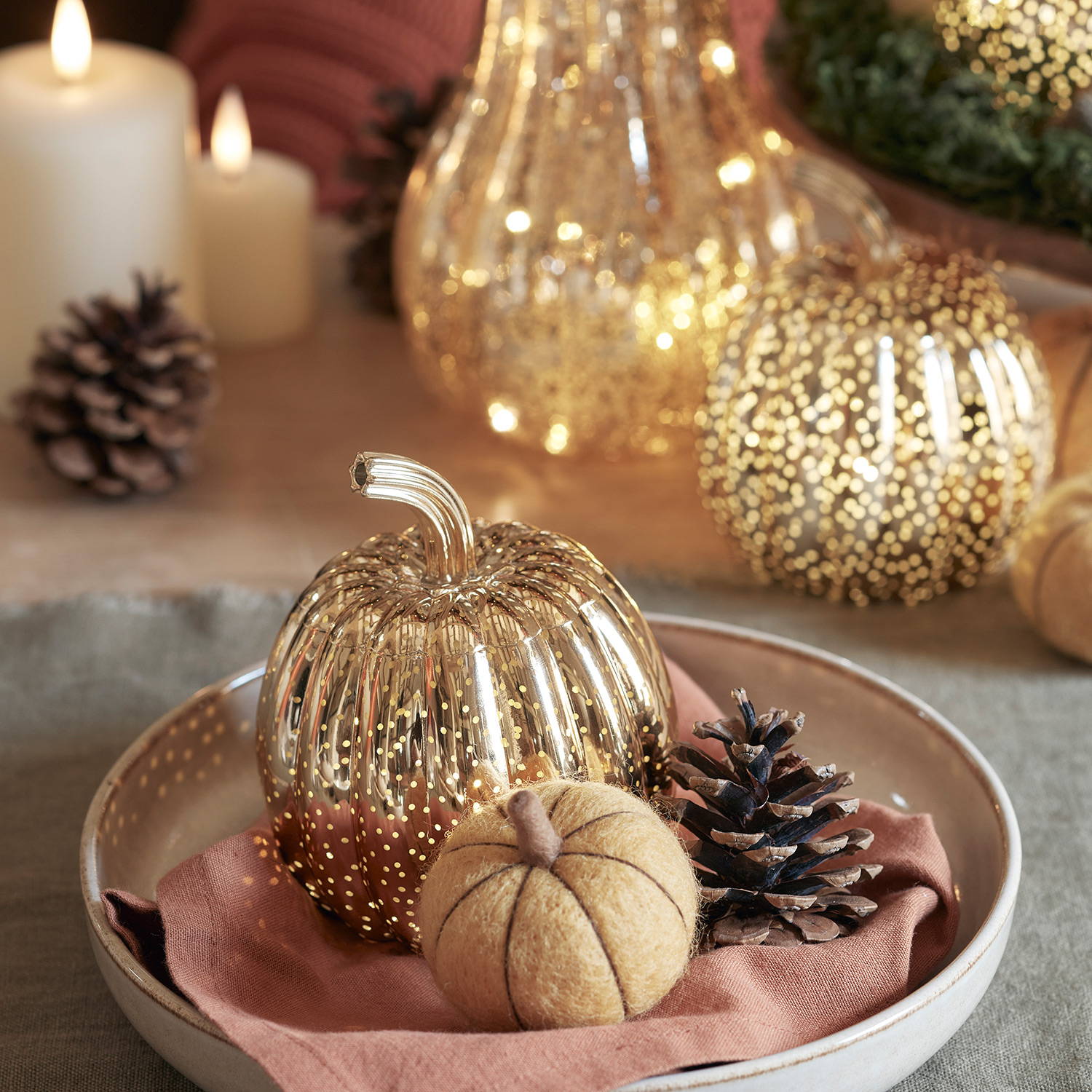 A mini brass pumpkin and felt pumpkin in a plate as a place setting for an autumnal dining display.