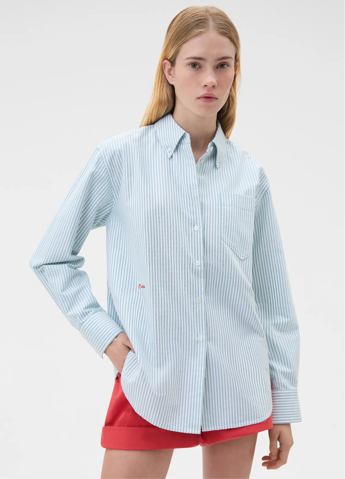 Model wearing a blue striped shirt and red shorts, standing against a light background.
