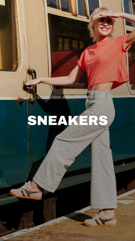 Smiling person in stylish outfit standing by a train, promoting sneakers.