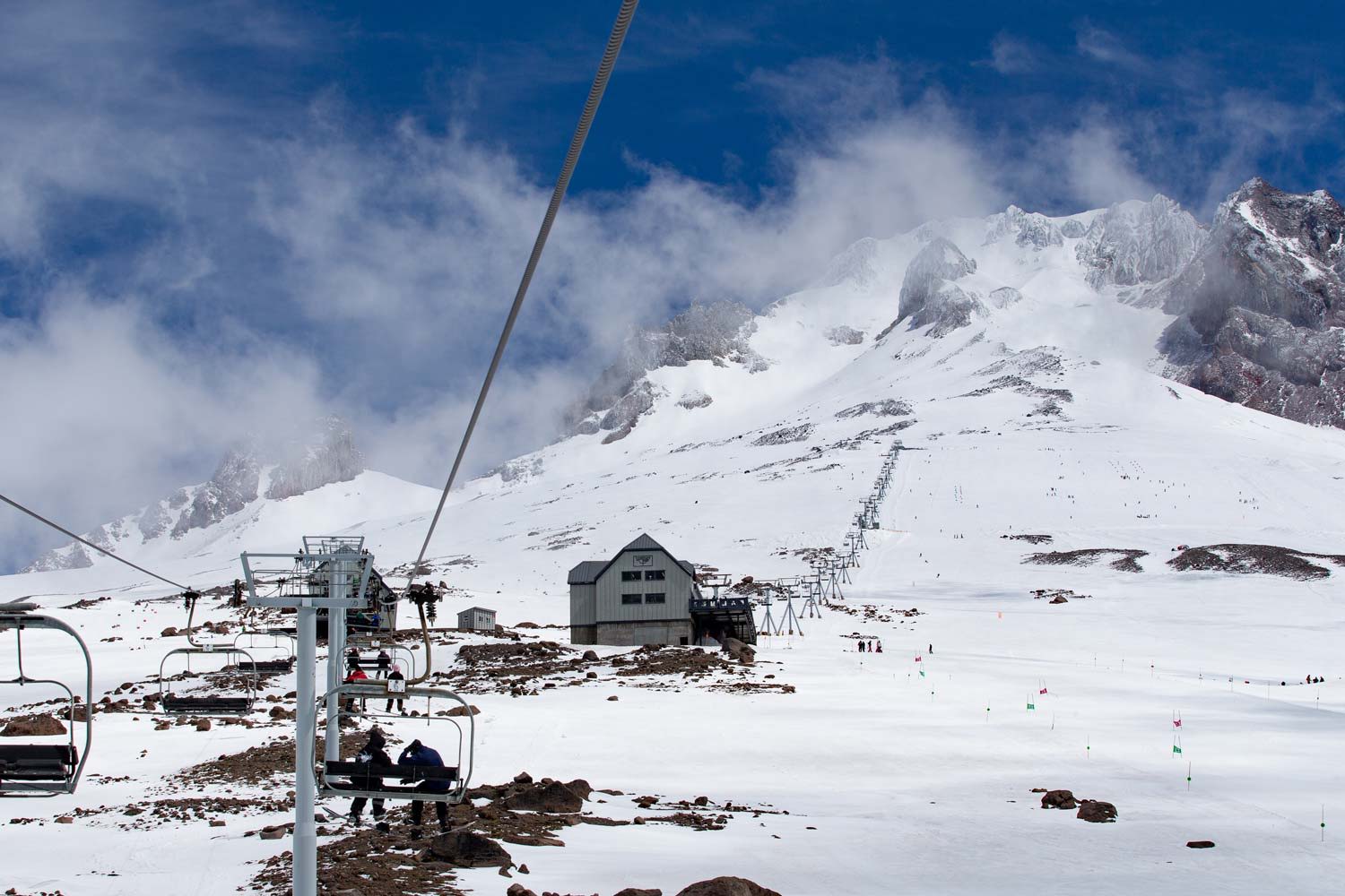 Ski resort with snowy mountains and a chairlift under a blue sky.