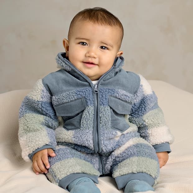 Baby in a cozy blue and gray outfit, smiling at the camera.