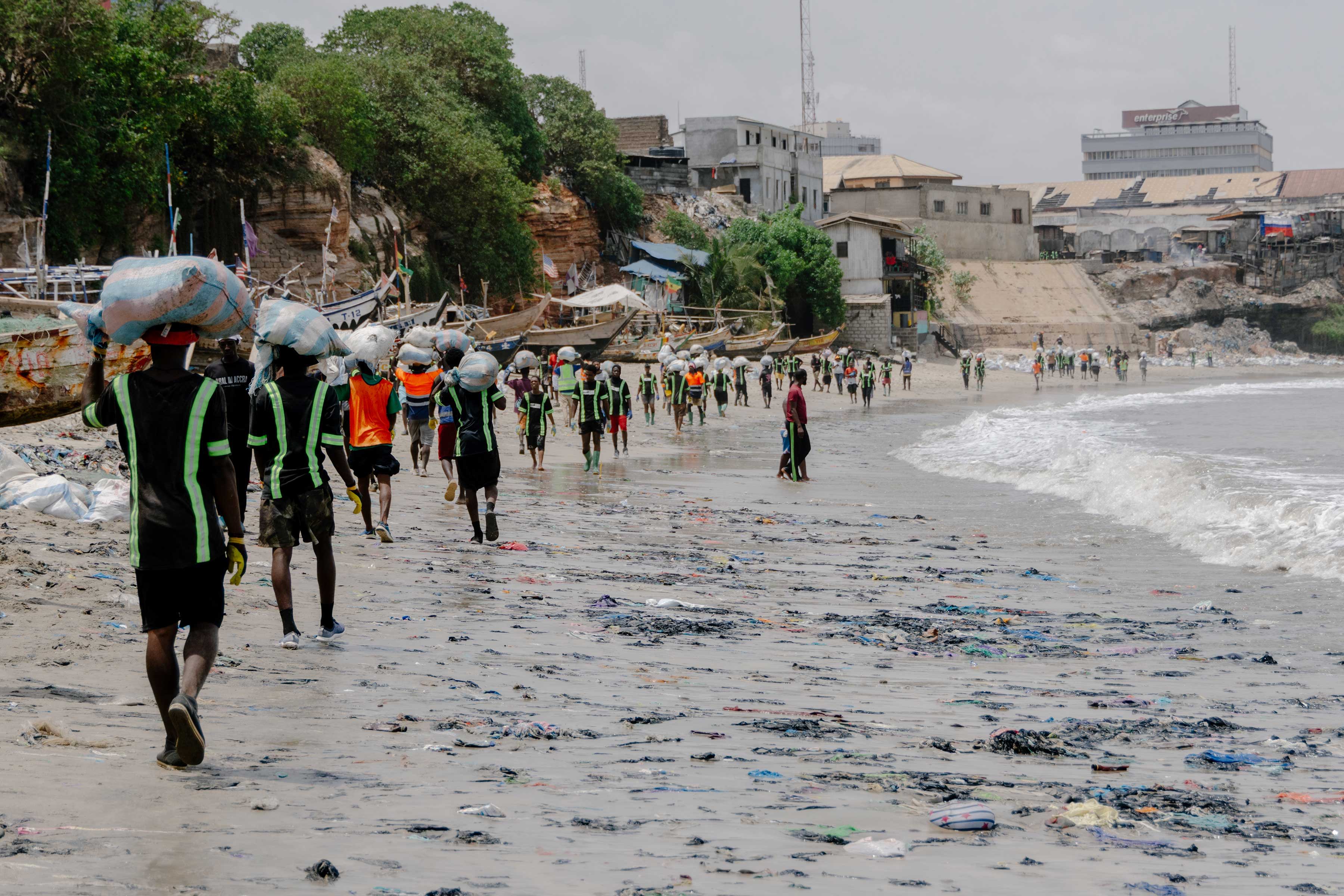 People walking along a beach littered with trash and debris.