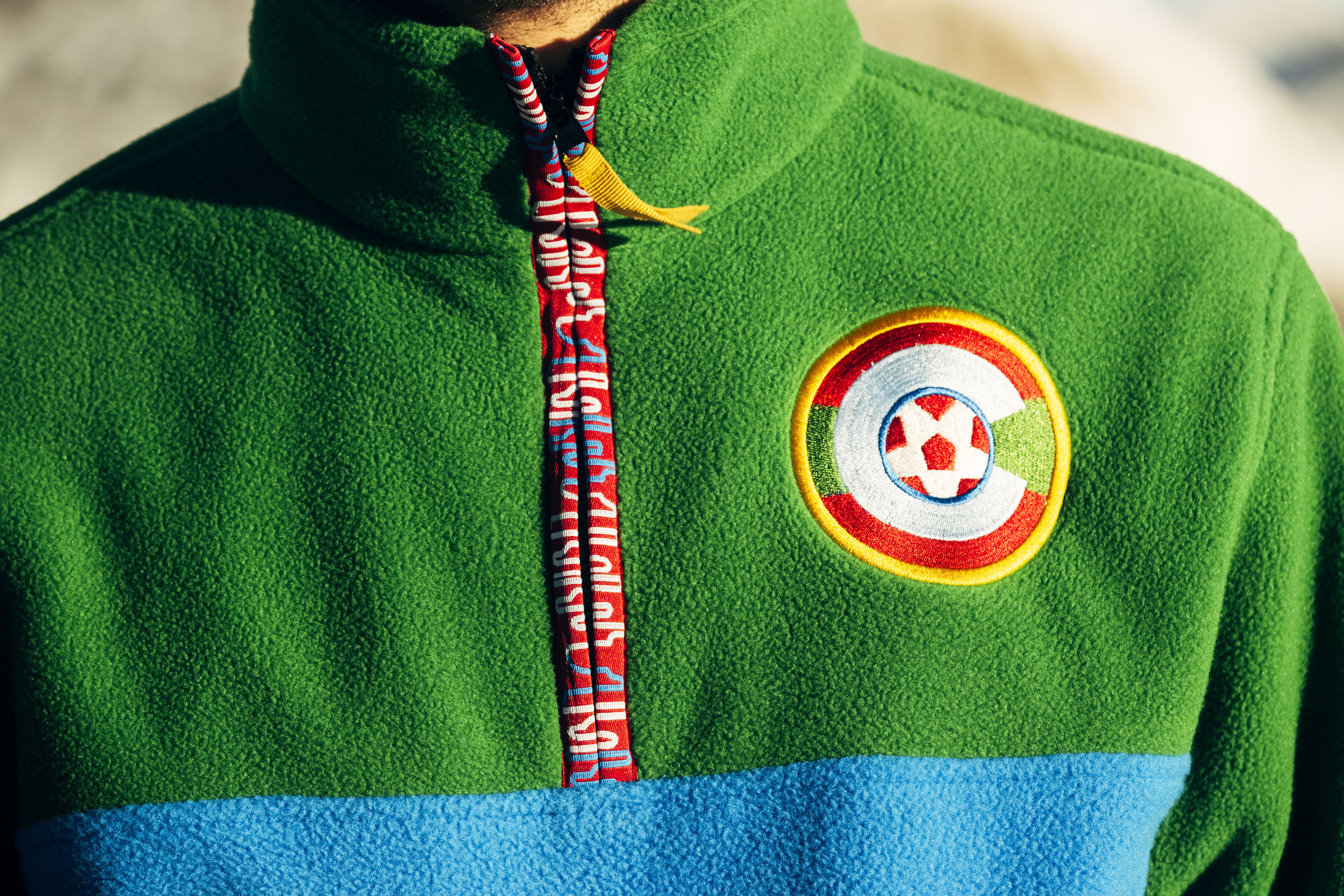 Person wearing a green and blue fleece jacket with a soccer-themed patch.