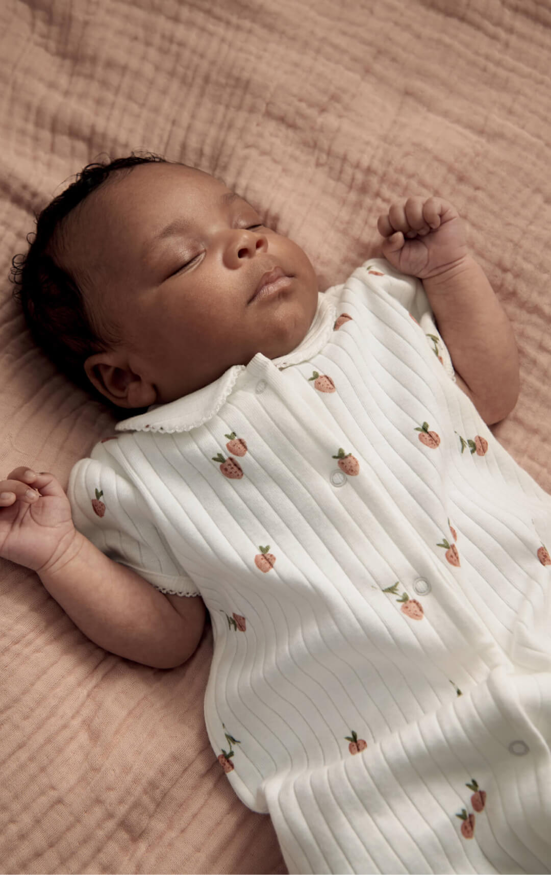 Sleeping baby in a white outfit with floral patterns on a soft blanket.