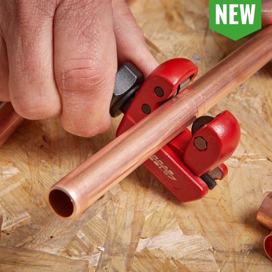 Person using a copper pipe cutter on a wooden surface.