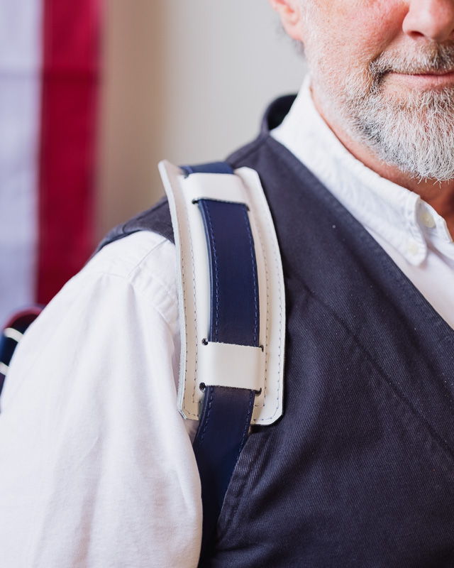 Close-up of a man's shoulder with a strap, American flag in background.