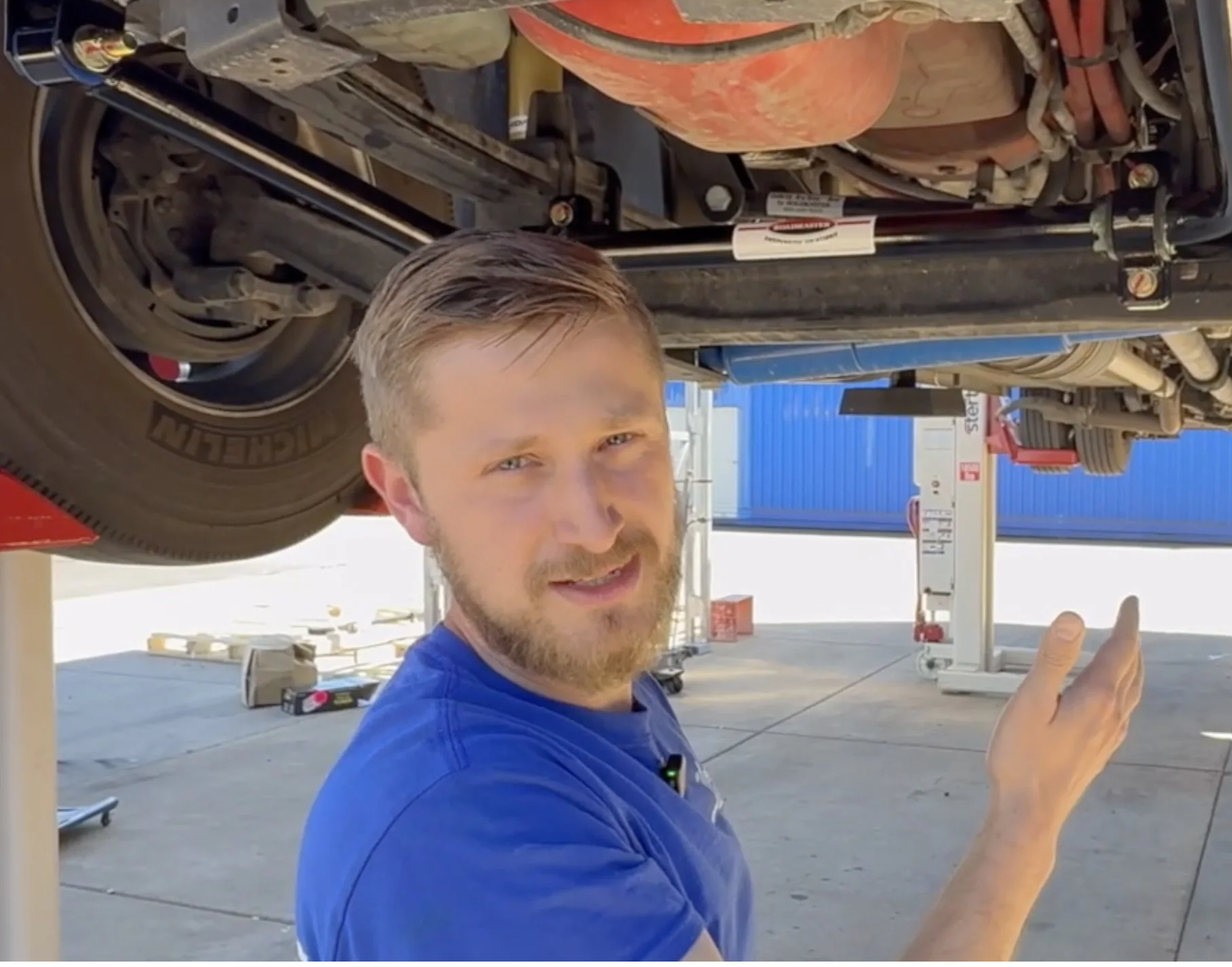 Mechanic working under a vehicle, pointing and explaining a component.