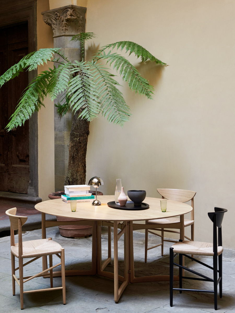 A wooden &Tradition HM6 Drop Leaf Extendable table with books and a plant in a modern setting.
