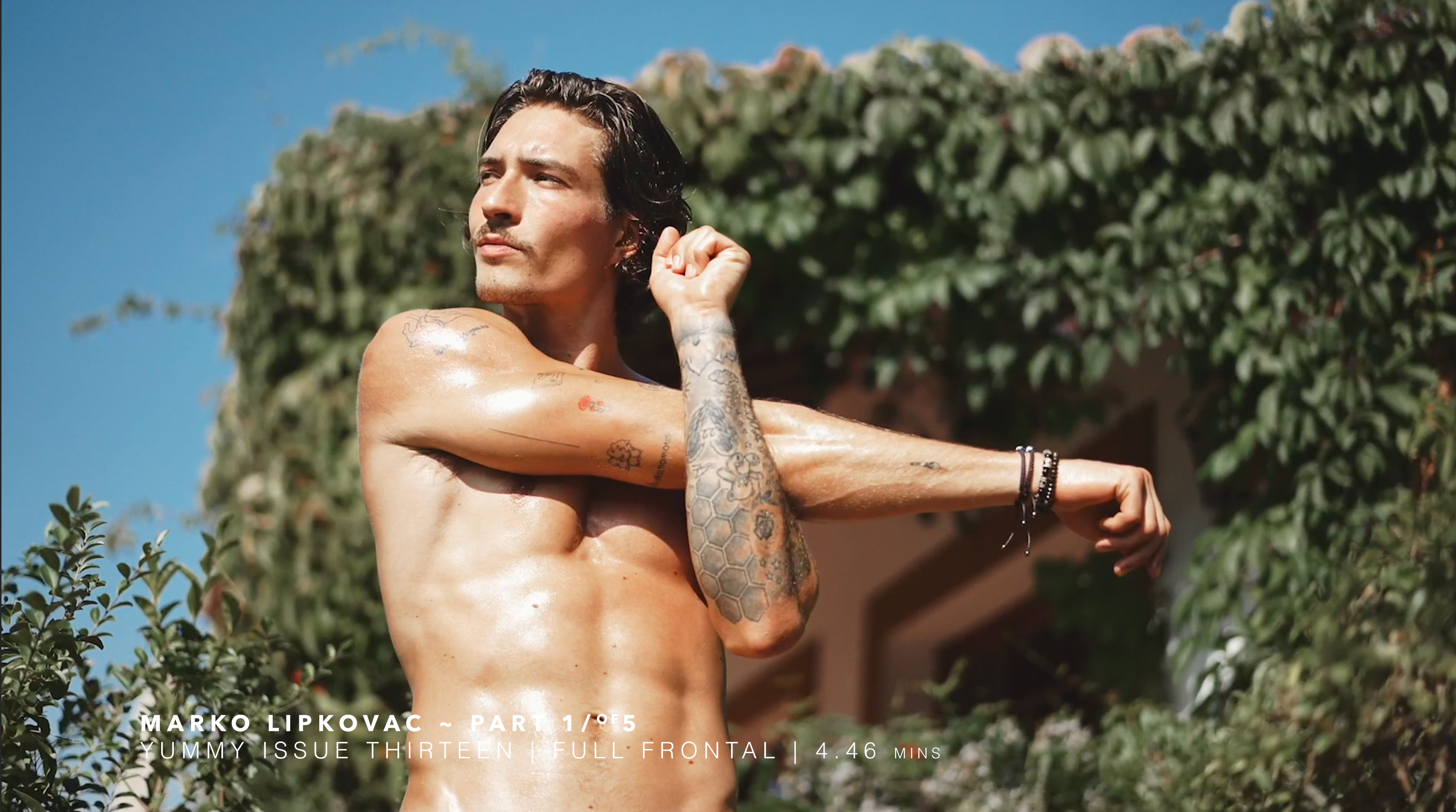 Man stretching outdoors, surrounded by greenery, with a muscular physique.