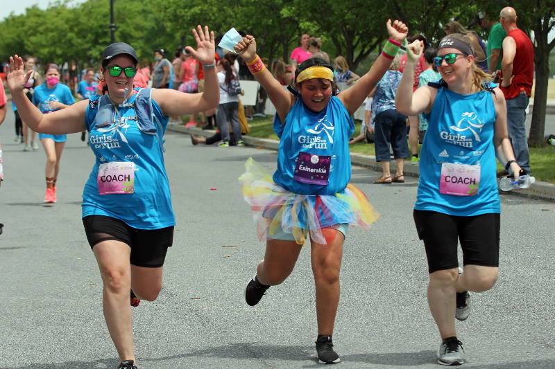 Two adults and a girl in a tutu crossing the finish line