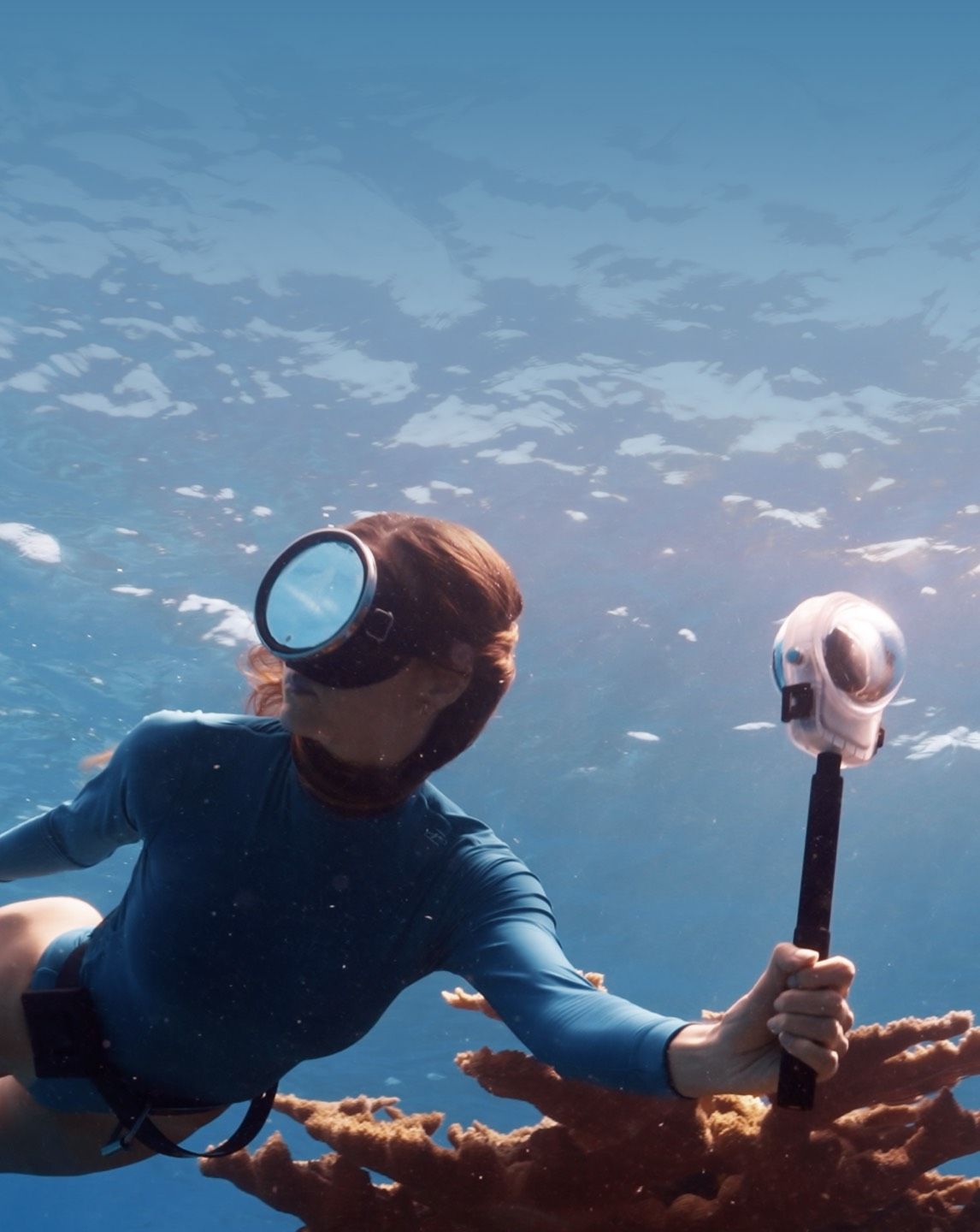 A person scuba diving underwater, holding a DJI Osmo 360 II camera with a waterproof cover.