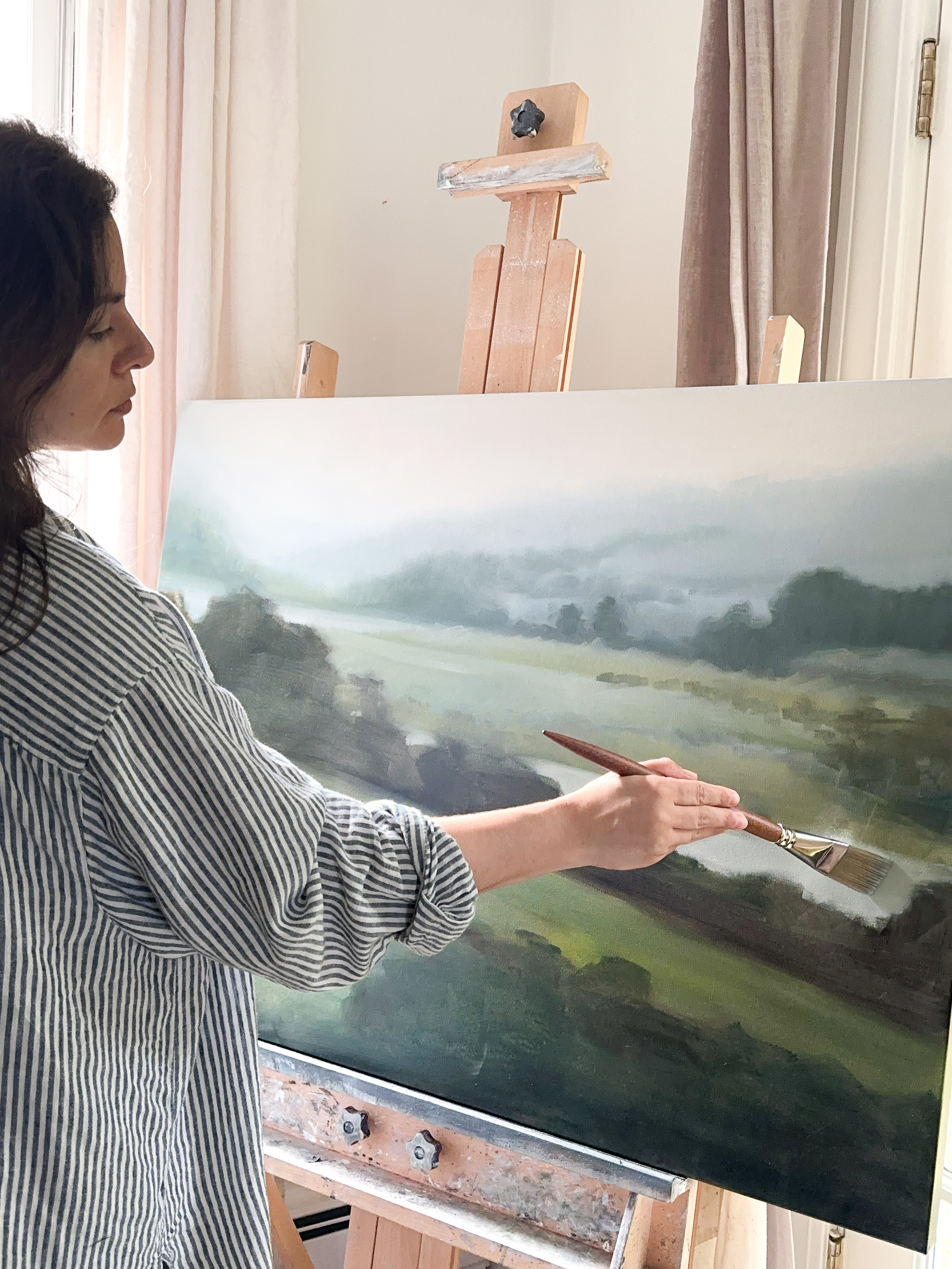 Artist Jess Blazejewski working on a countryside landscape painting in her studio