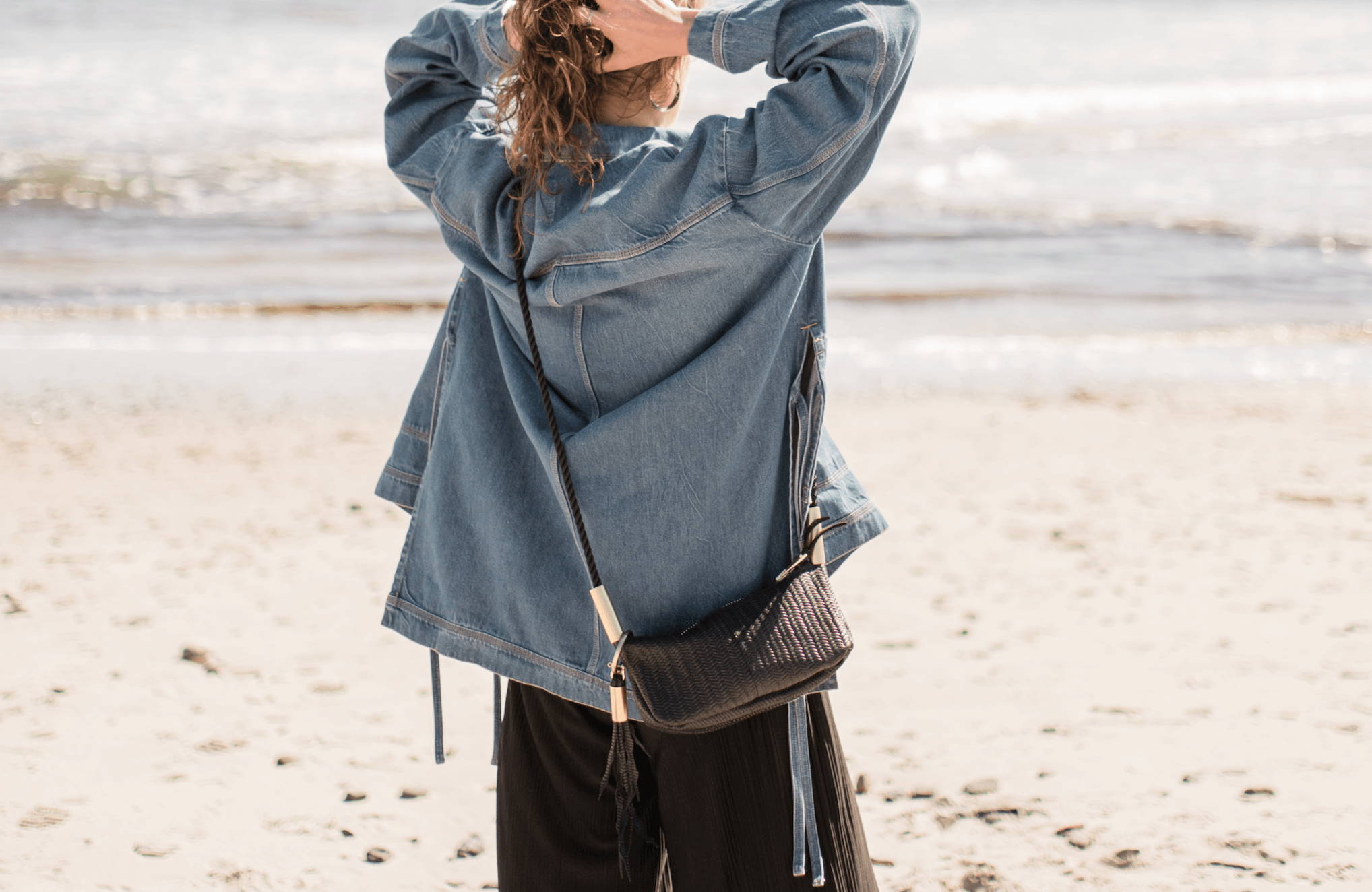 woman looking at the the ocean with a black basketweave bag