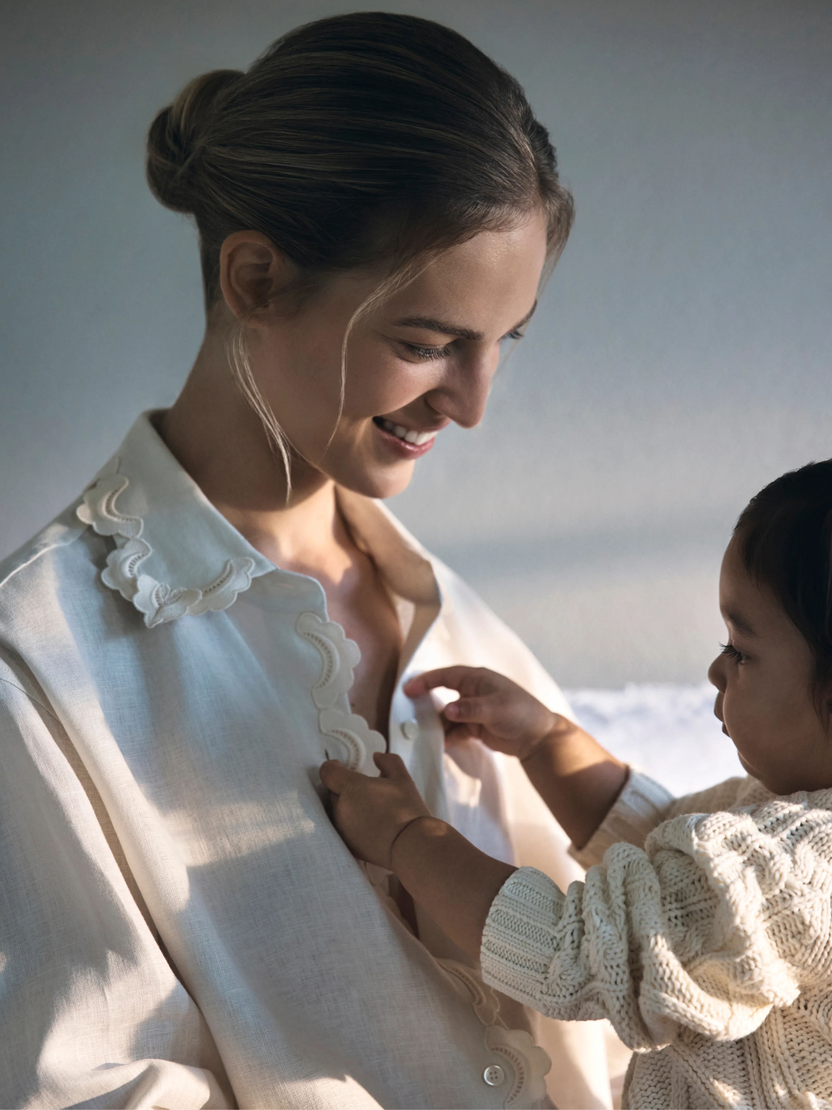 A woman smiles as a child touches her shirt.