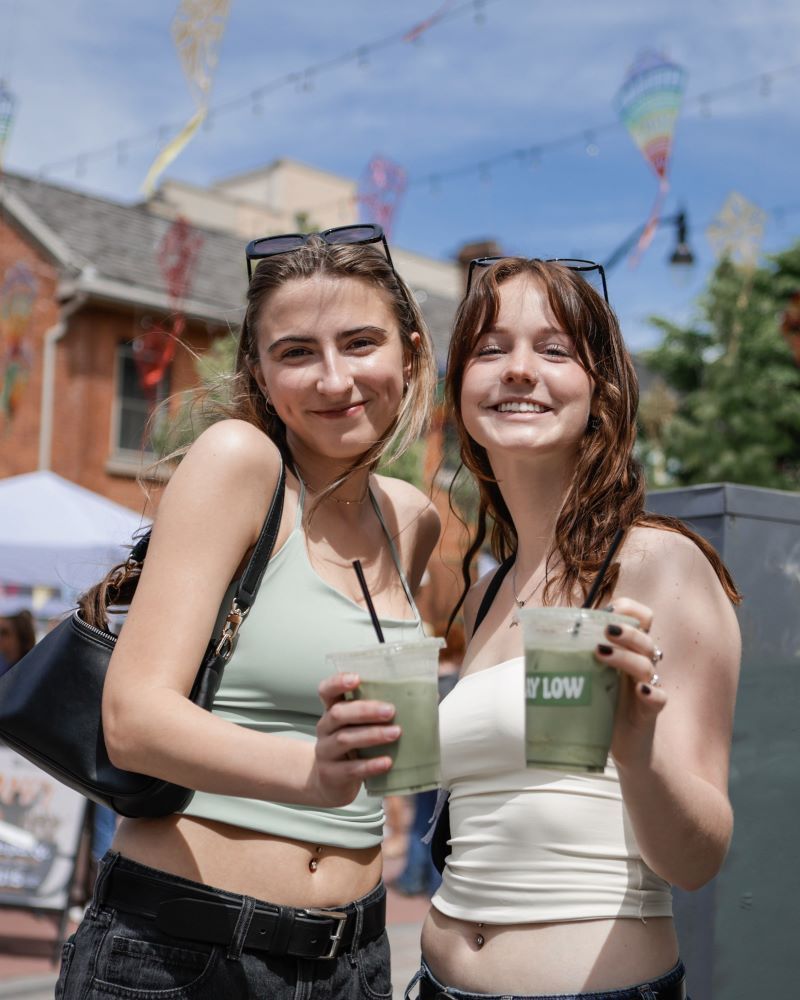 Two smiling women holding drinks outdoors on a sunny day.
