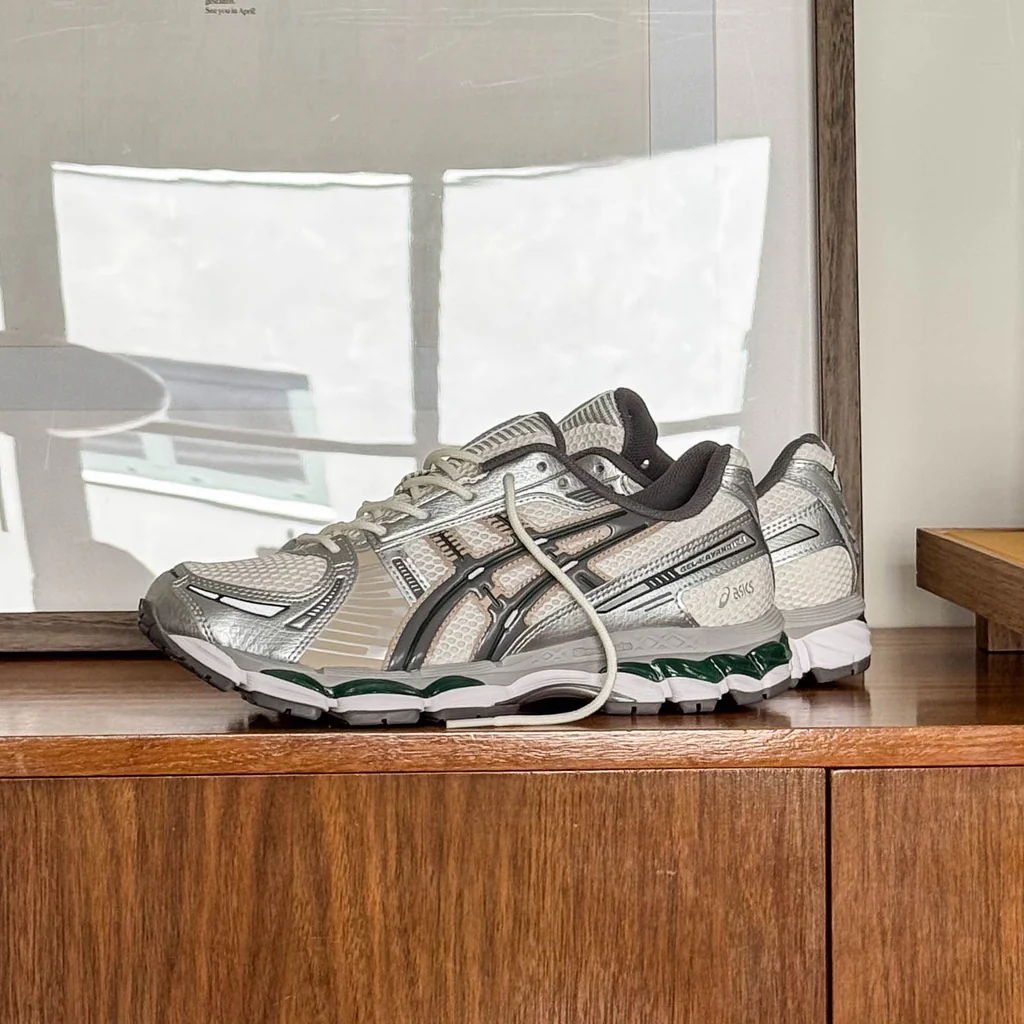 A silver athletic shoe displayed on a wooden surface near a framed picture.