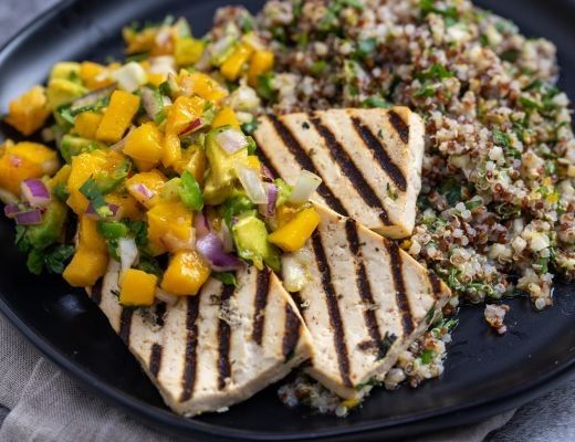 Grilled tofu with mango salsa and quinoa on a black plate.