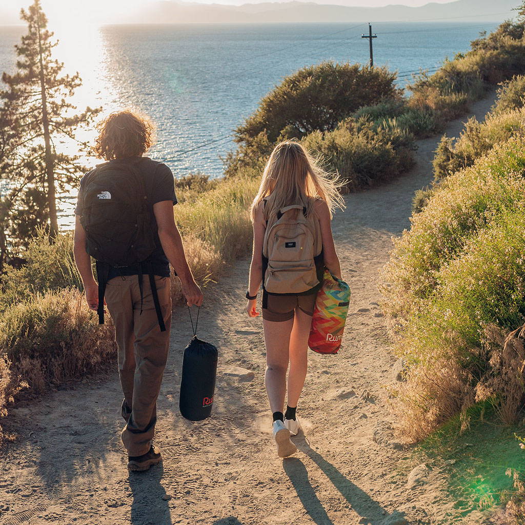 Two friends walking on a path by the sea with packed Rumpl blankets in hand.