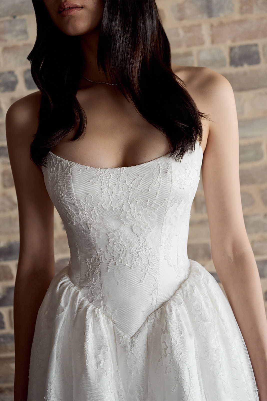 Woman in a white wedding dress against a brick wall background.