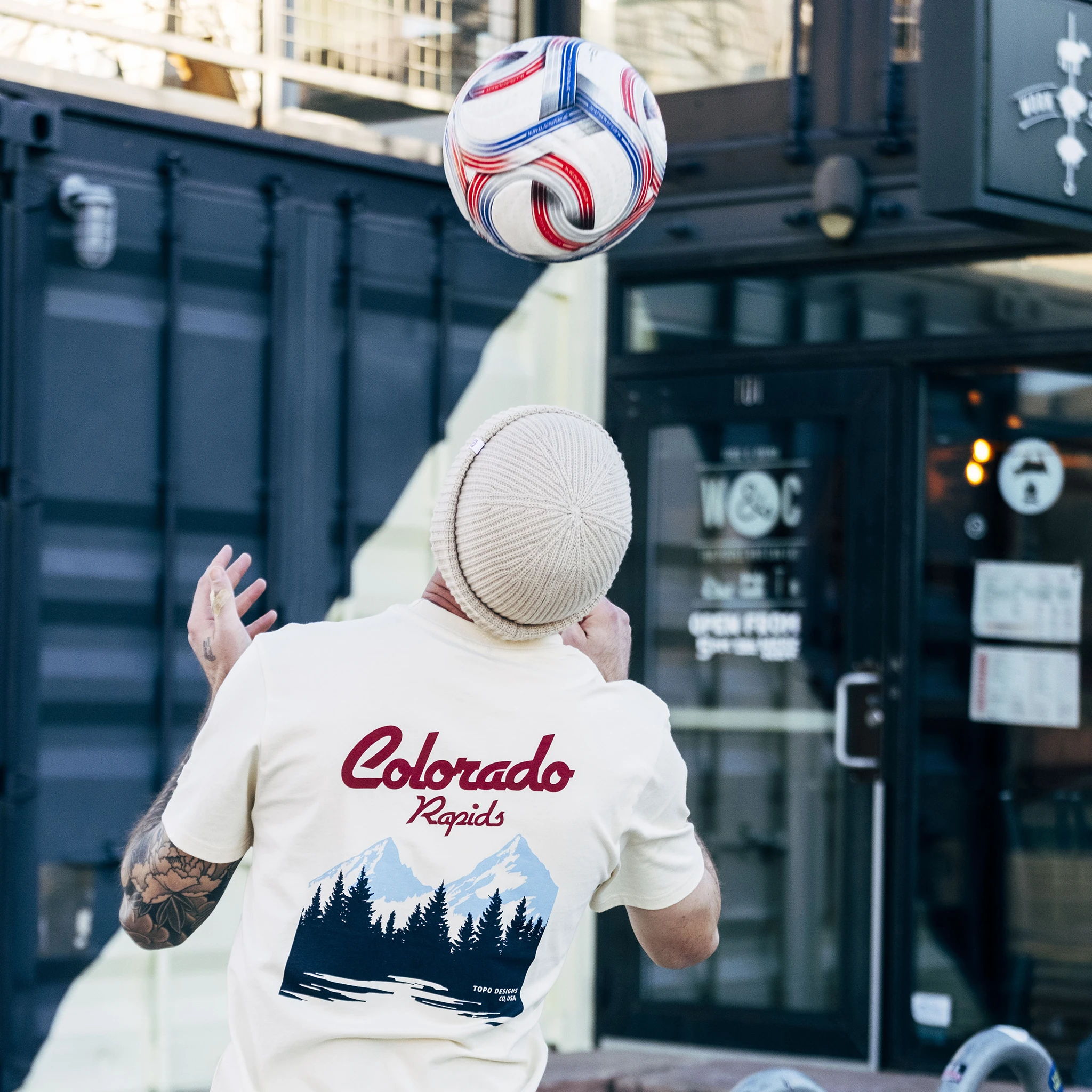 Person in a Colorado Rapids shirt juggling a soccer ball outdoors.