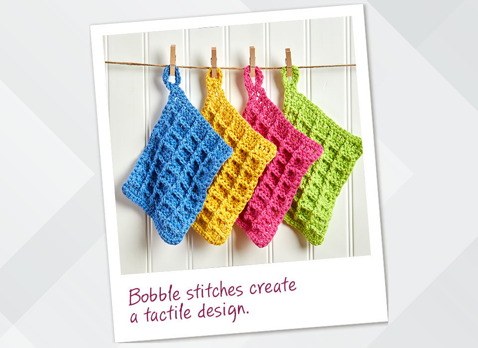 Colorful knitted dishcloths hanging on a line with bobble stitch design.