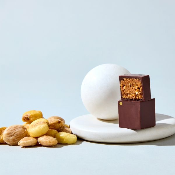 Chocolate dessert next to nuts and a white sphere on a plate.