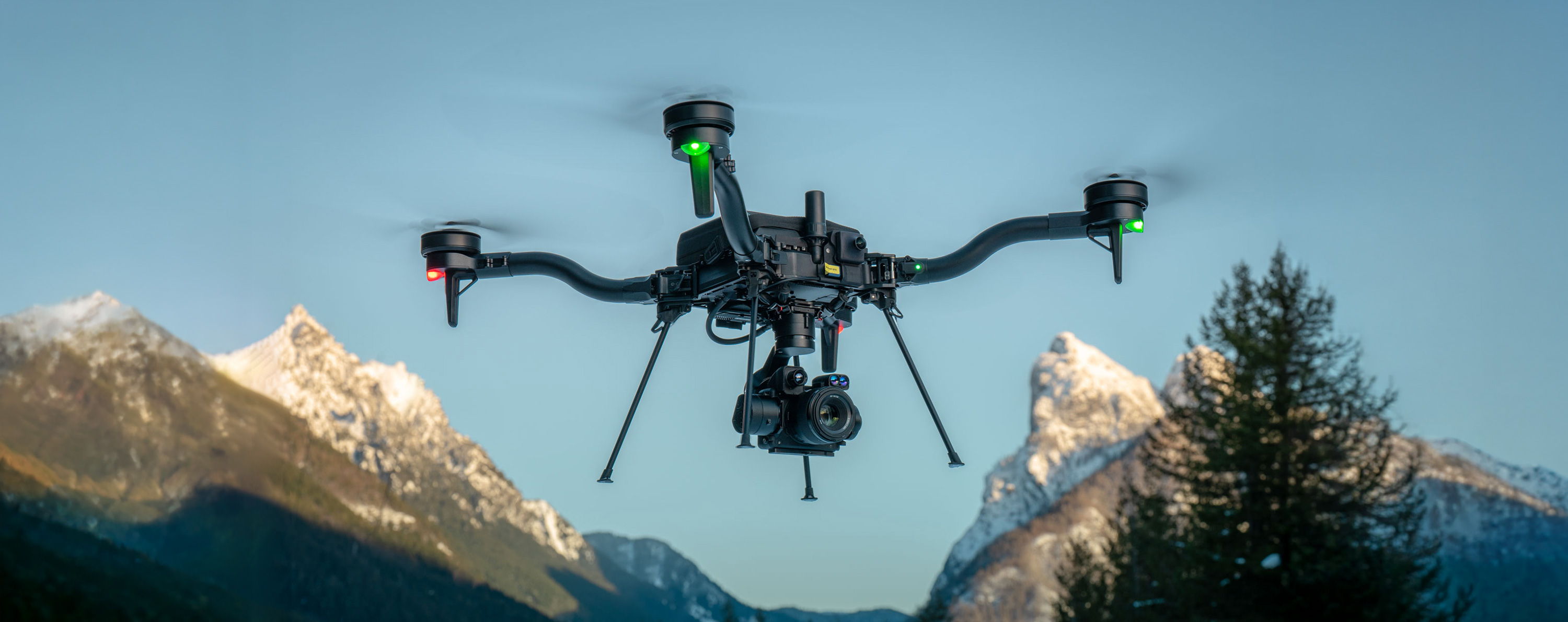 Un drone Freefly Astro volant au-dessus de montagnes sous un ciel bleu clair.