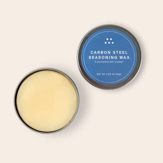 An open tin of Misen Carbon Steel Seasoning Wax seen from above, with beige wax and blue-and-white lid label visible.