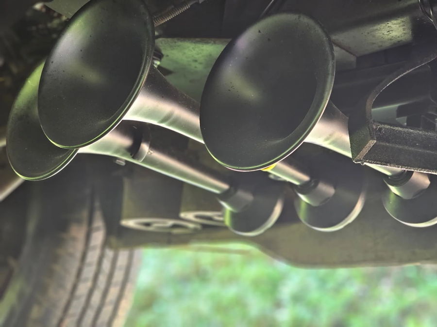 Low-angle four matte black train horn trumpets undercarriage mounting bracket tire grass Brandon's Dodge B350 Flatlaw 3 Liter gallery photo 3