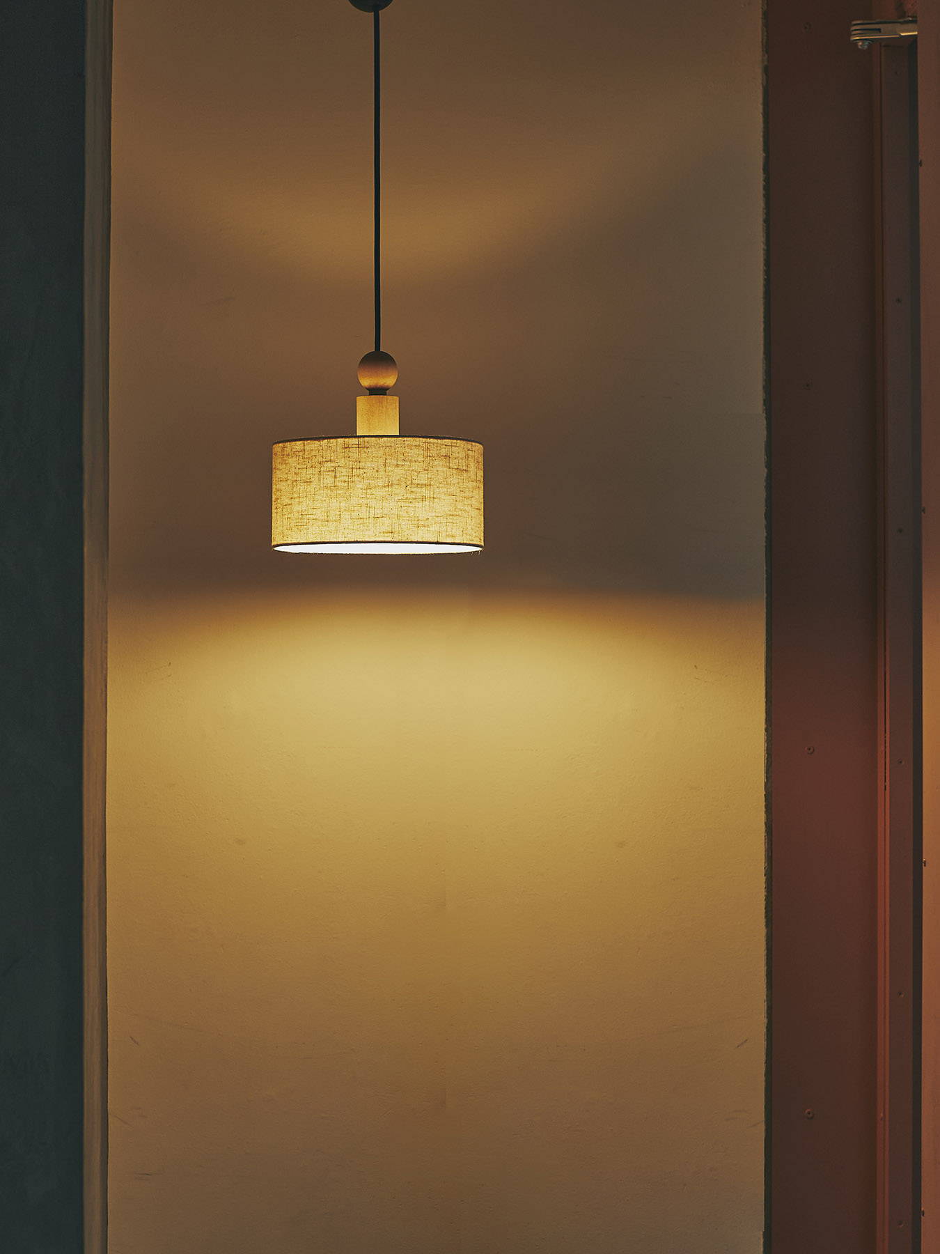 A pendant light hanging against a softly lit wall.