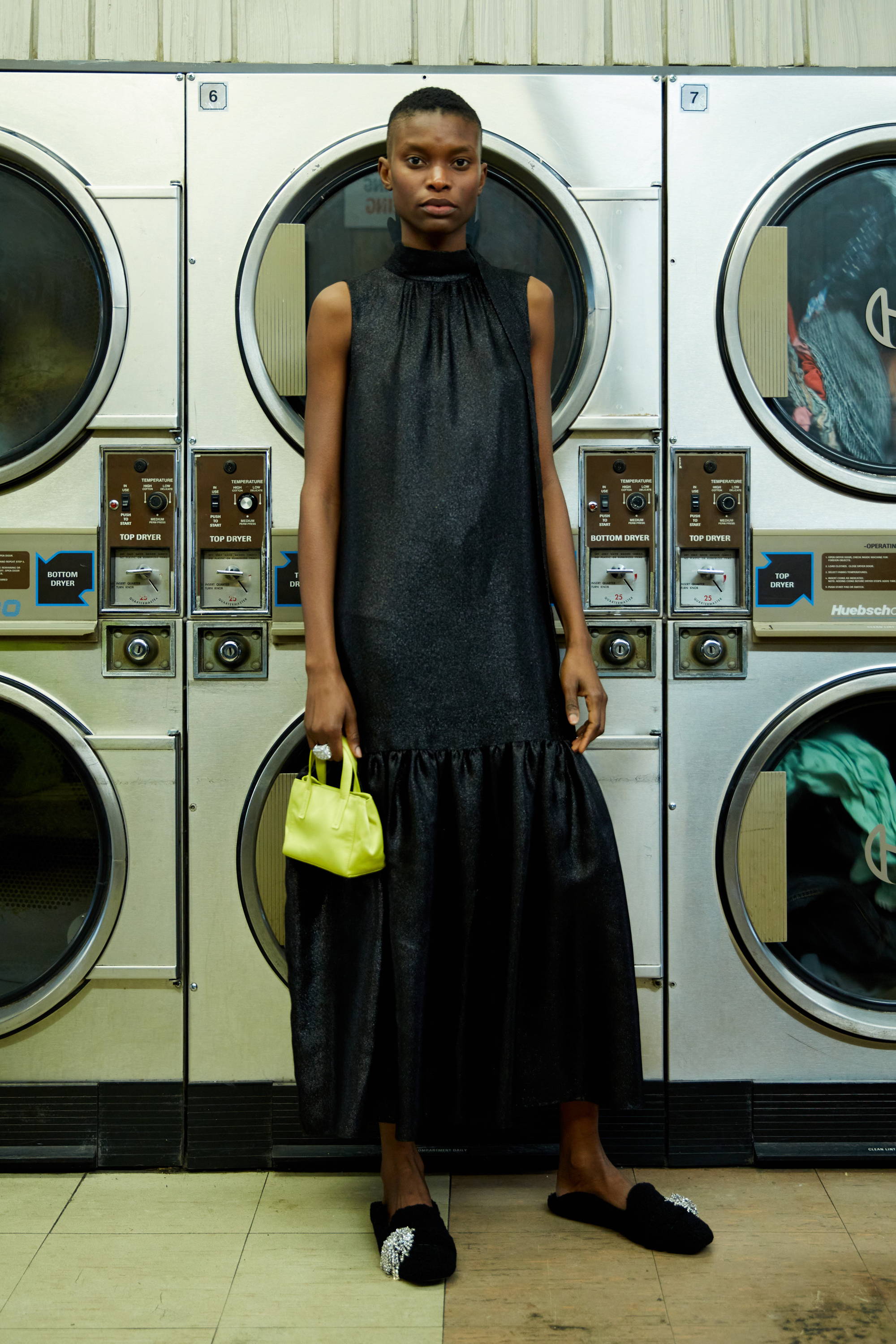 Person in a black dress holding a yellow bag in a laundromat.