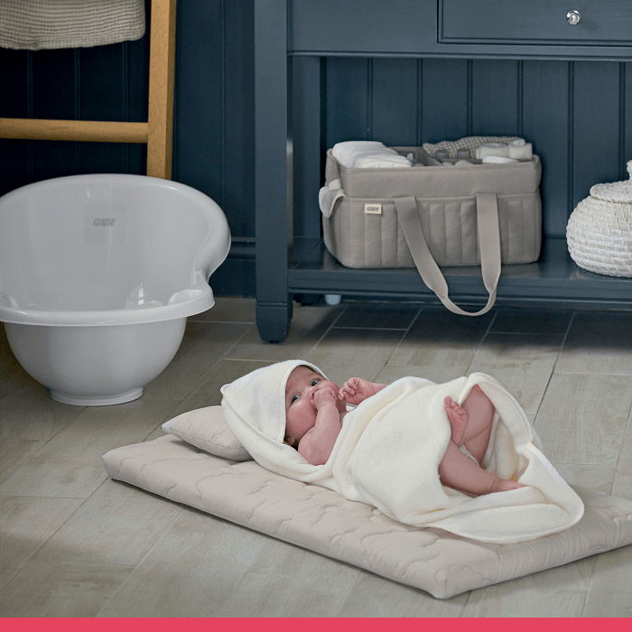 A baby wrapped in a blanket lies on a mat in a nursery.