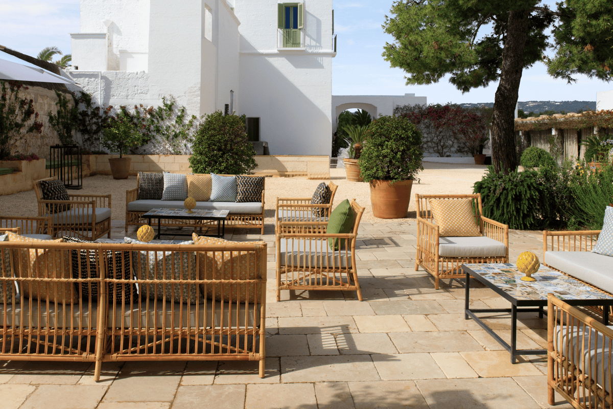 Low-maintenance outdoor lounge area with natural woven furniture, neutral cushions, stone pavers, and large container plants