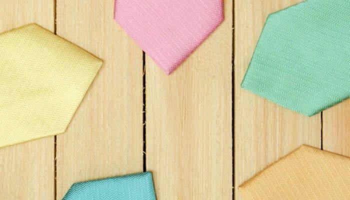 The tips of pastel herringbone neckties in yellow, pink, seafoam, gold and turquoise on top of a wood backdrop