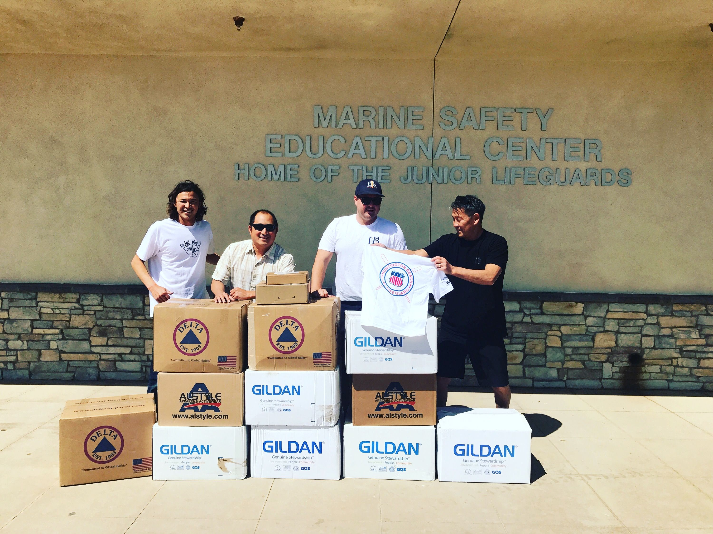 4 people standing in front of Marine Safety Center with boxes of t-shirts