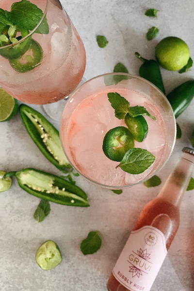 Overhead shot of non-alcoholic rosé jalapeño  mocktail in a coupe glass. There are fresh jalapeños scattered around the base of the glass.