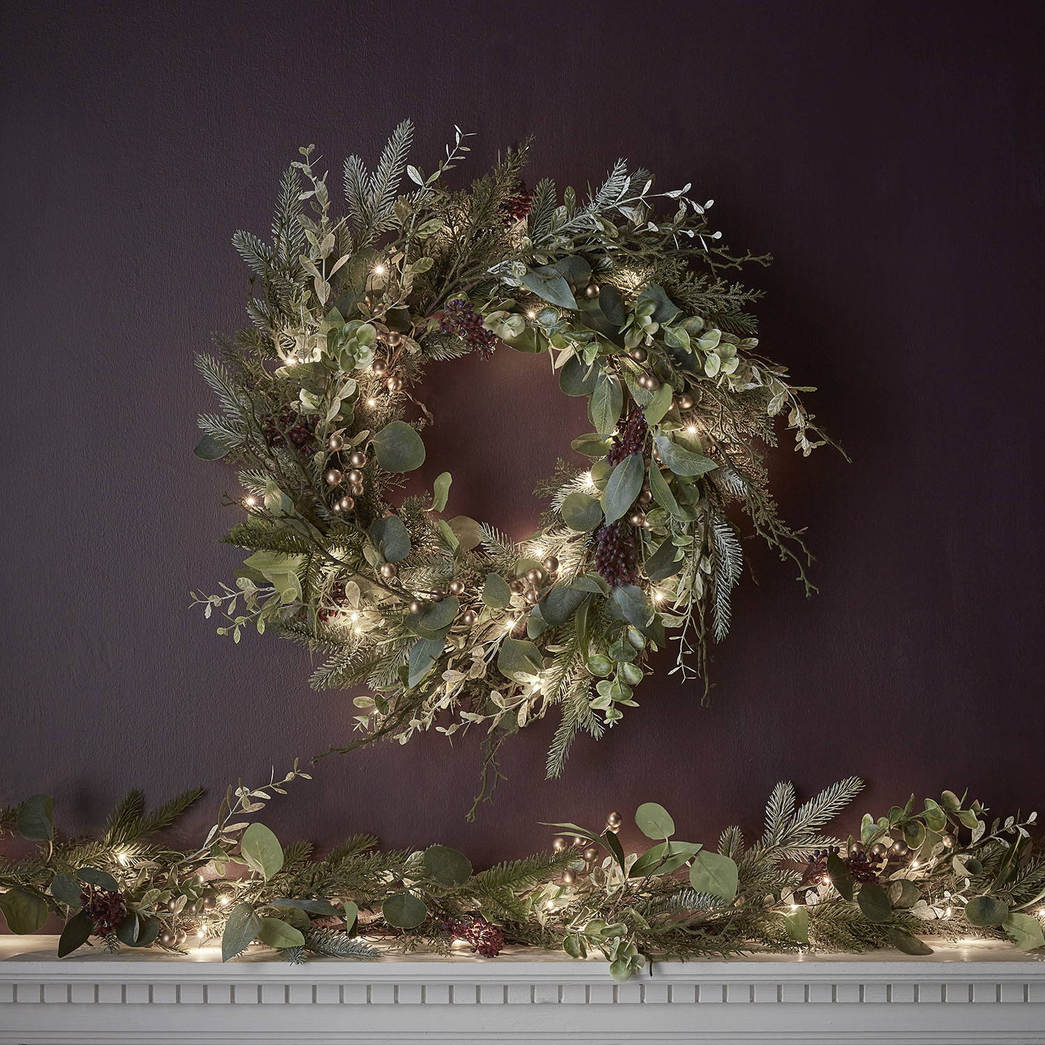 A gold berry, and LED lit wreath and matching garland adorning a mantlepiece 