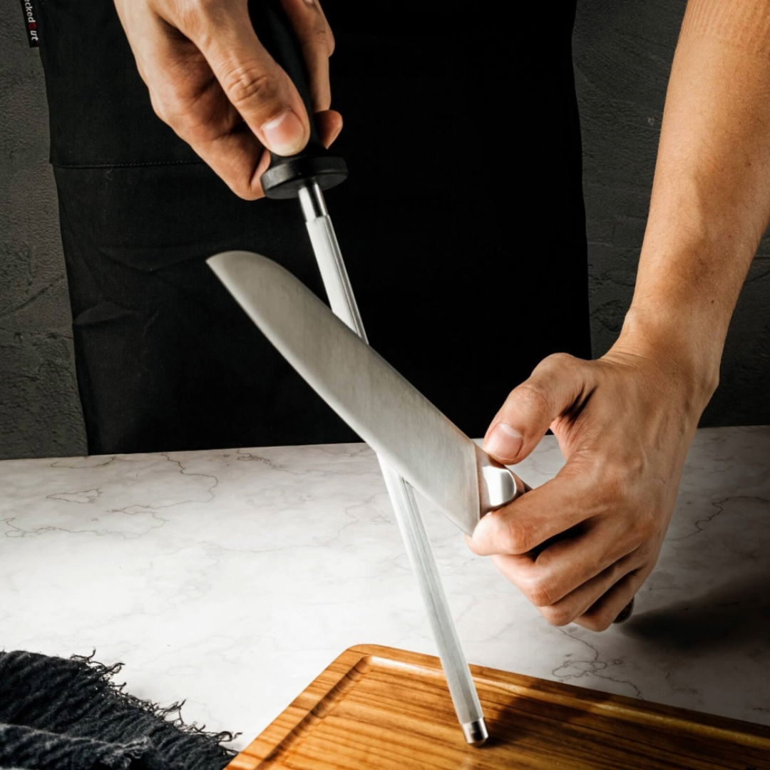 A person sharpening a knife with a honing steel on a wooden cutting board.