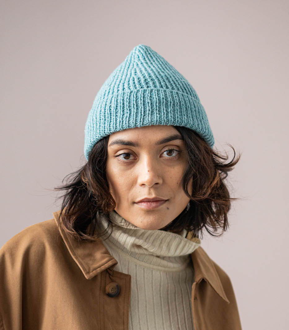 A female model wearing a ribbed watchcap with a peaked crown.